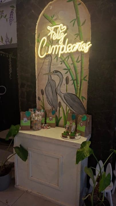 Mesa de souvenirs de cumpleaños con cartel neón Feliz Cumpleaños, mural de garzas y bolsitas temáticas