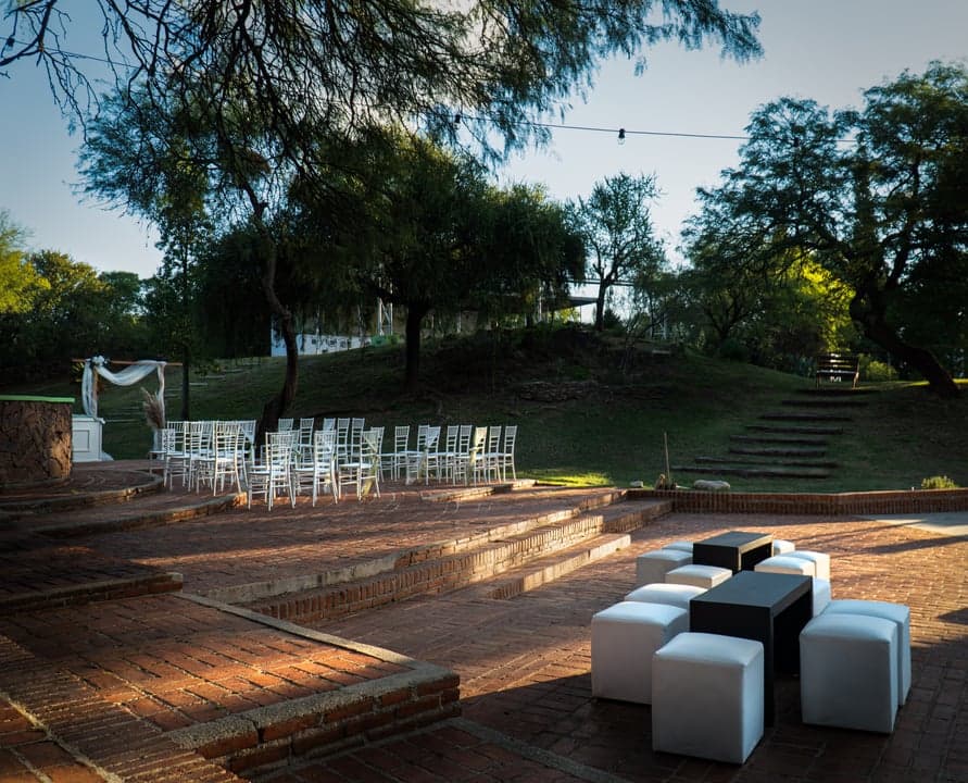 Vista panorámica del parque exterior con altar, puffs lounge y salón iluminado de fondo